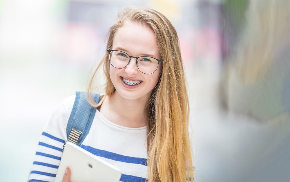 Smiling school girl wearing braces and carrying a school bag
