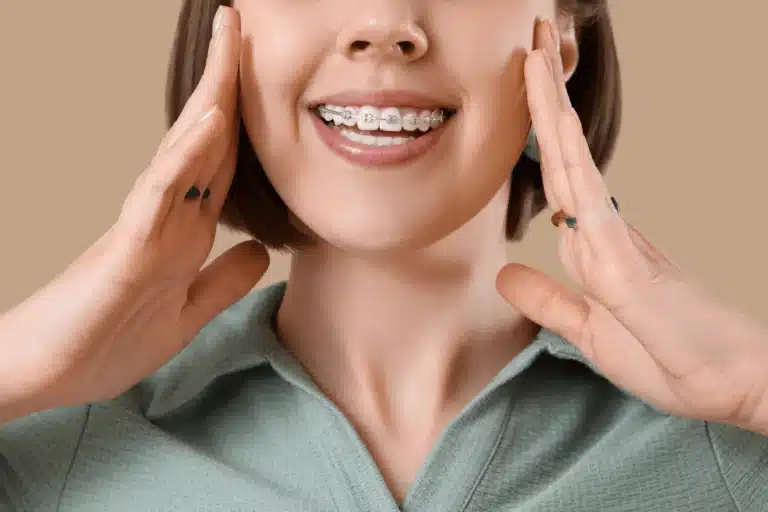 Adult smiling with metal braces on their teeth while touching both sides of their face.
