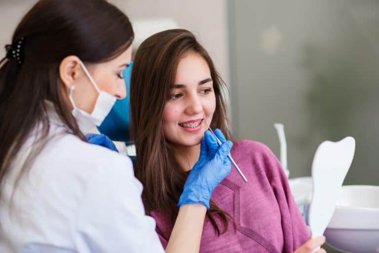 Orthodontist examining a teenage patient’s braces with a dental mirror during an orthodontic appointment.